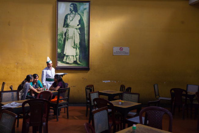 ©Stuart Freedman, A waiter serves schoolgirls beneath a portrait of Rabindranath Tagore in the Indian Coffee House, Kolkata, 2013, C-type print - Courtesy Tasveer