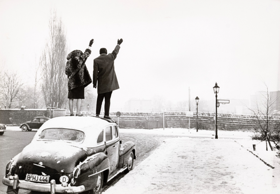 &quot;Noêl à Berlin. A l'angle d'une rue enneigée depuis Bergstrasse, un couple debout sur le toit d'une voiture lève le bras pour saluer de l'autre côté du mur vers Berlin Est, Berlin&quot;, 1961 © Paris, musée de l'Armée / Emilie Cambier / Léon Herschtritt/ LA COLLECTION