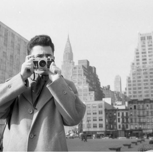 Bob Lerner for LOOK magazine, Hungarian Refugee [Man with a camera standing with his back to the United Nations Building], January 31, 1957, Museum of the City of New York. Gift of Cowles Magazines, Inc, X2011.4.7087-57